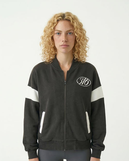 Woman wearing a black jacket with white stripes and a logo on a plain background