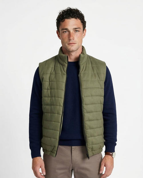 Man wearing a green puffer vest over a navy shirt on a white background