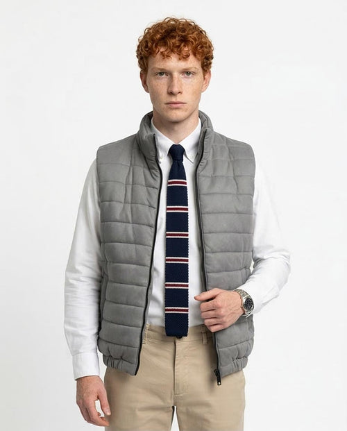 Man wearing a gray puffer vest over a white shirt with a striped tie on a light gray background