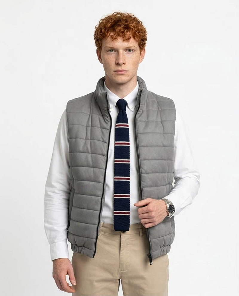 Man wearing a gray puffer vest over a white shirt with a striped tie on a light gray background