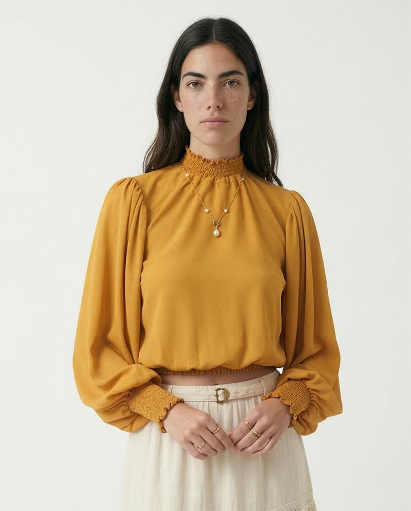 Woman wearing a mustard yellow blouse with long sleeves on a white background