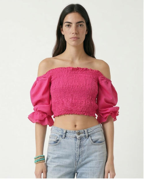 Woman wearing a bright pink off-shoulder top and light blue jeans on a white background