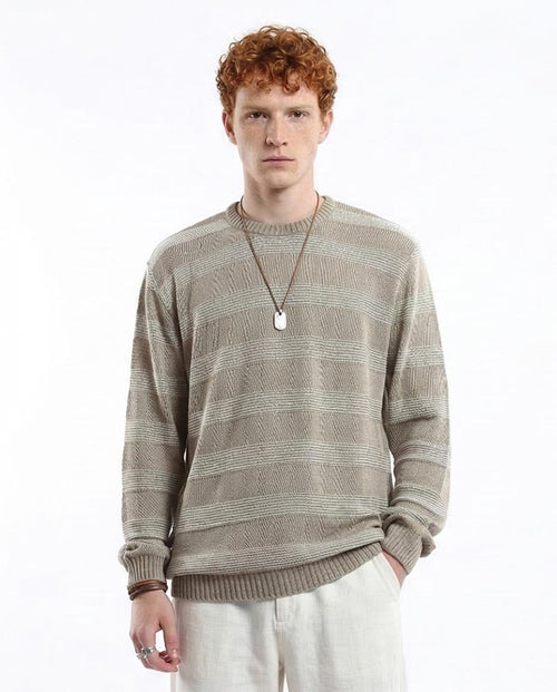 Man wearing a patterned sweater and light pants on a white background