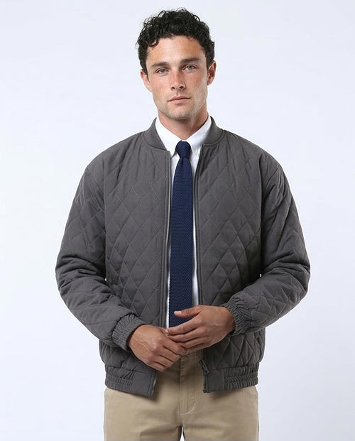 Man wearing a gray quilted jacket over a white shirt with a blue tie on a white background