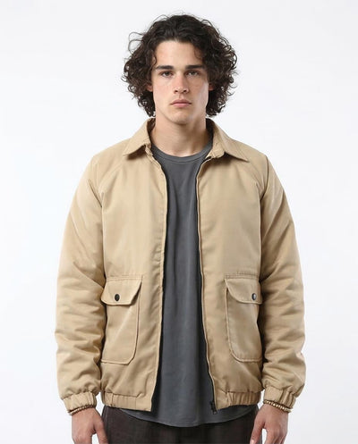 Man wearing a beige jacket over a gray shirt on a white background