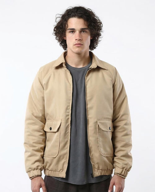 Man wearing a beige jacket over a gray shirt on a white background