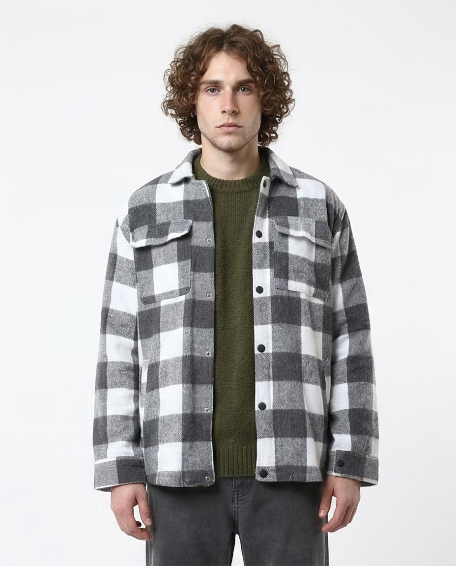 Man wearing a gray and white checkered shirt over a green sweater on a white background