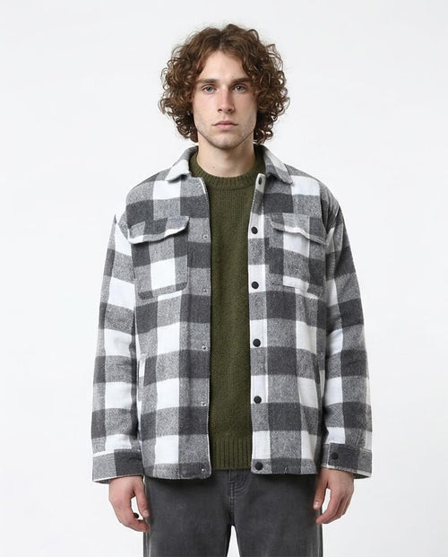 Man wearing a gray and white checkered shirt over a green sweater on a white background