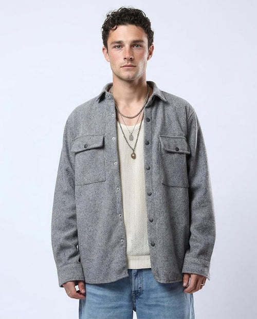 Man wearing a gray jacket over a beige sweater with a plain background