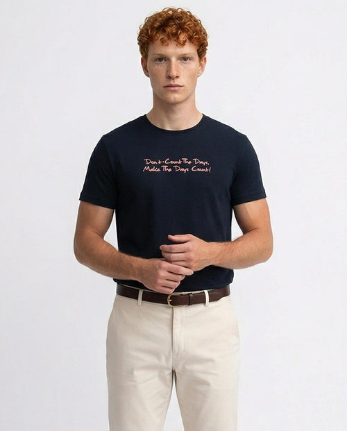 Man wearing a navy t-shirt with text and beige pants on a white background