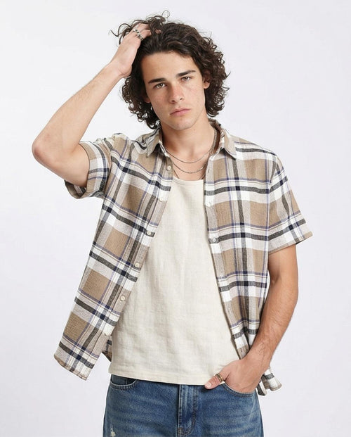 Man wearing a plaid shirt over a white t-shirt with blue jeans on a light gray background