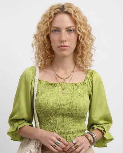 Woman wearing a green top with ruffled sleeves against a white background