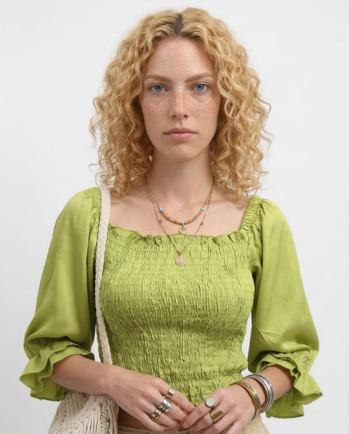 Woman wearing a green top with ruffled sleeves against a white background