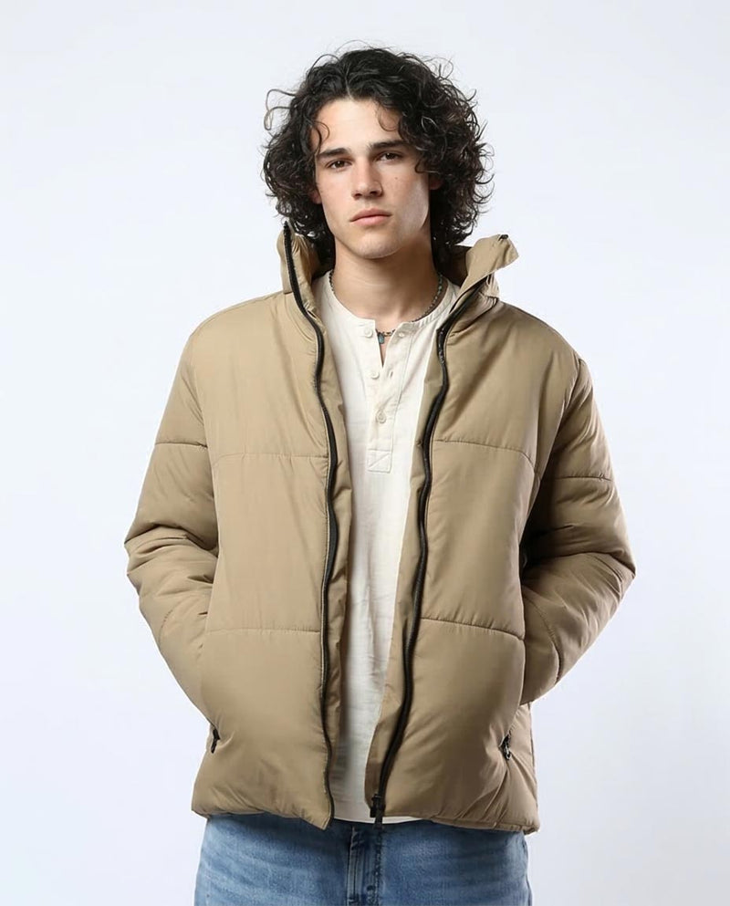 Man wearing a beige puffer jacket over a white shirt on a light gray background