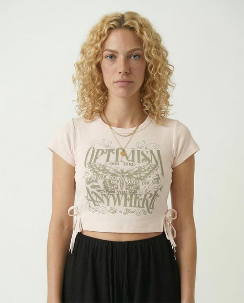 Woman wearing a light pink crop top with text design on a plain background