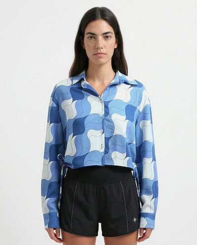 Woman wearing a blue and white patterned shirt with black shorts on a light gray background