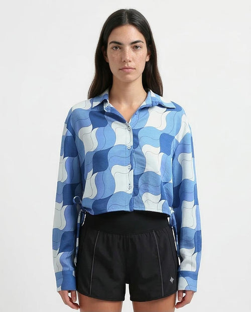 Woman wearing a blue and white patterned shirt with black shorts on a light gray background