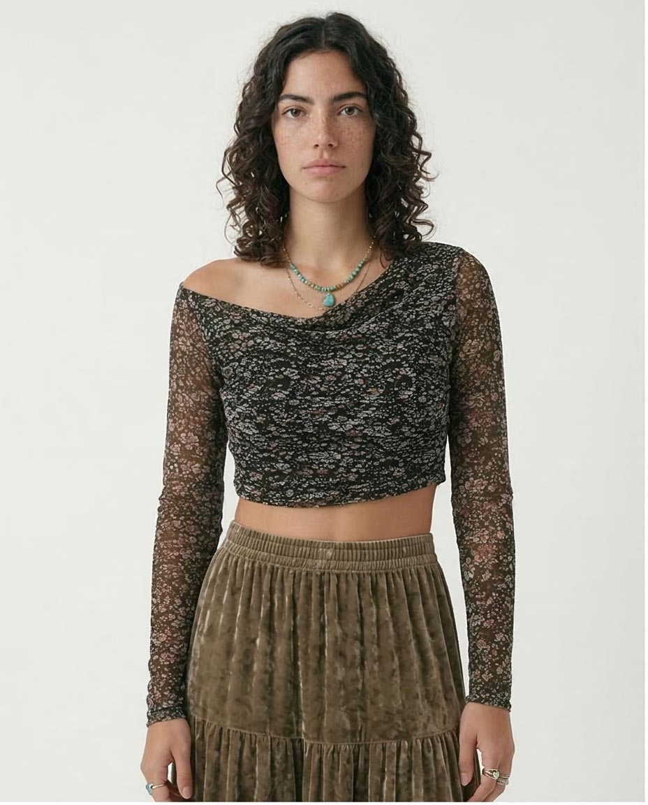 Woman wearing a black and gold patterned top with sheer sleeves and a brown pleated skirt on a white background