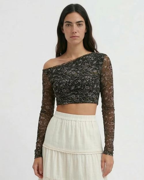 Woman wearing a black floral lace top with long sleeves and a white skirt on a white background