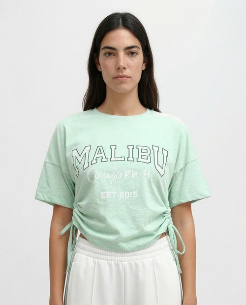 Person wearing a light green 'Malibu' t-shirt with a white background
