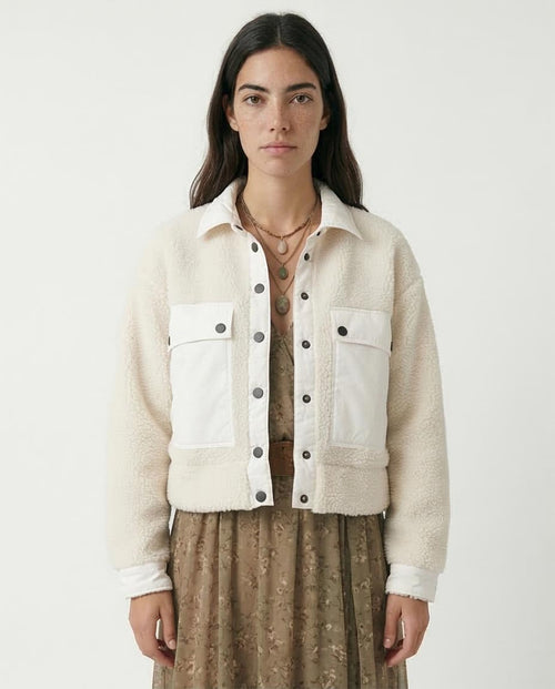 Woman wearing a cream-colored jacket with black buttons on a white background