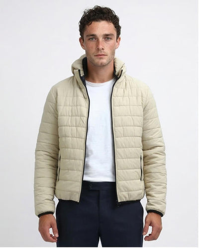 Man wearing a beige quilted jacket over a white shirt on a light gray background