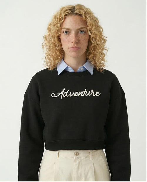 Woman wearing a black sweatshirt with 'Adventure' text on a plain background