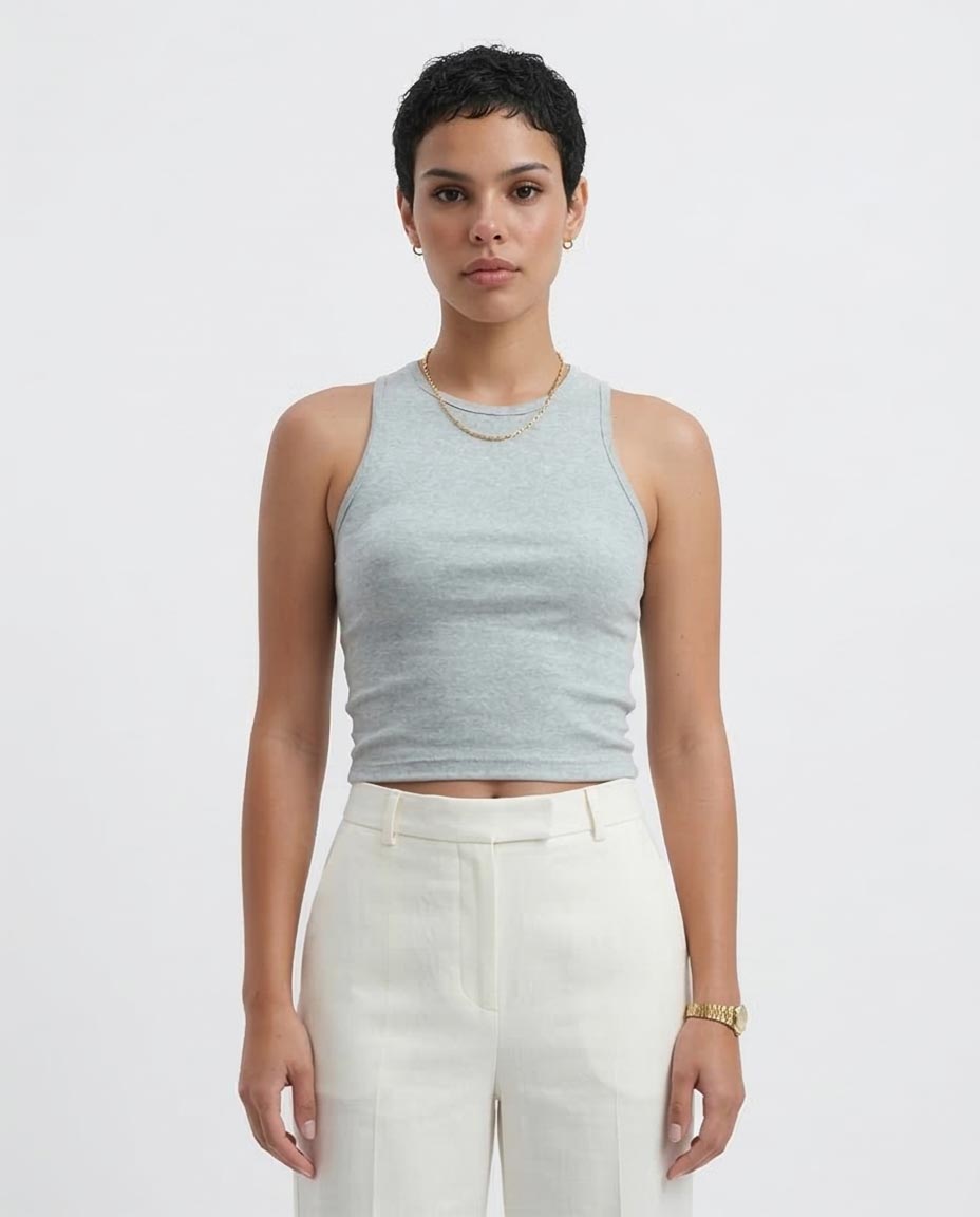 Woman wearing a light gray sleeveless top and white pants on a plain background