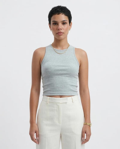 Woman wearing a light gray sleeveless top and white pants on a plain background