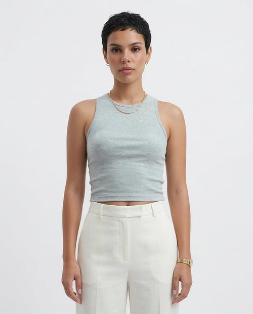 Woman wearing a light gray sleeveless top and white pants on a plain background