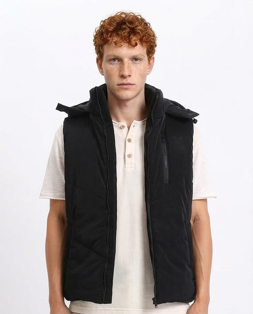 Man wearing a black vest over a white shirt on a light gray background