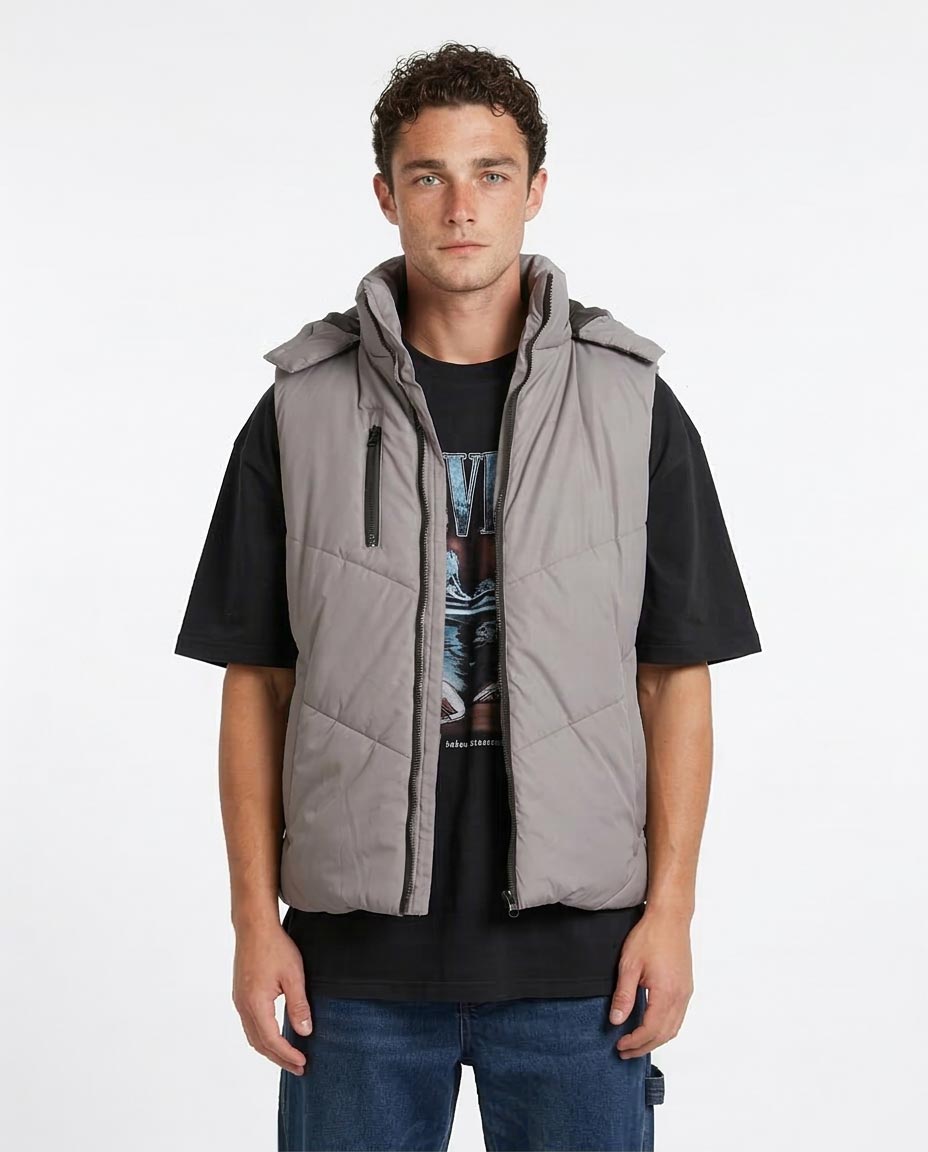 Man wearing a gray quilted vest over a black shirt on a white background