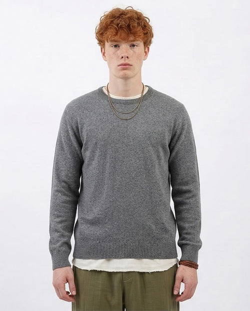 Man wearing a gray sweater over a white shirt with a plain background