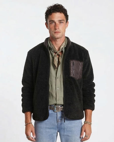 Man wearing a black jacket over a green shirt with blue jeans on a white background