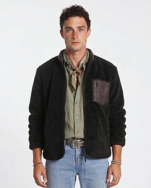 Man wearing a black jacket over a green shirt with blue jeans on a white background