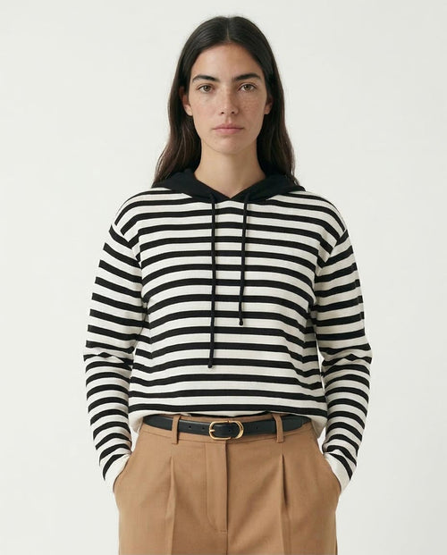 Person wearing a black and white striped hoodie with beige pants on a plain background