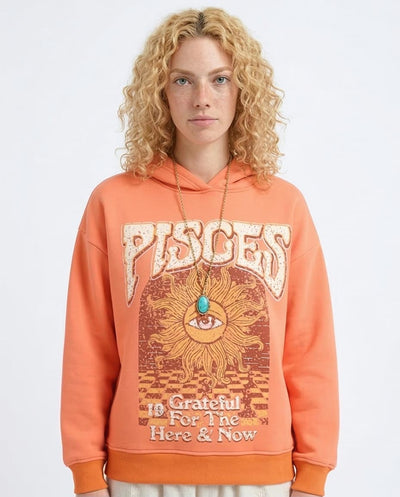 Woman wearing an orange hoodie with 'Pisces' and celestial design on a plain background