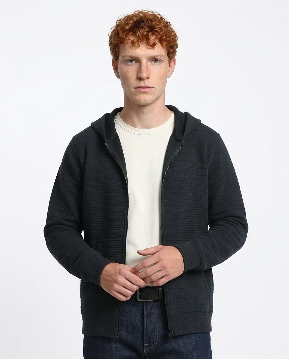 Man wearing a black zip-up hoodie over a white shirt on a light gray background