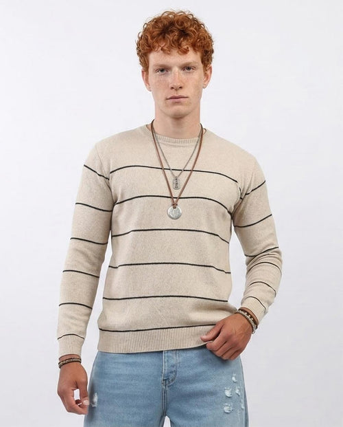 Man wearing a beige striped sweater and light blue jeans against a white background