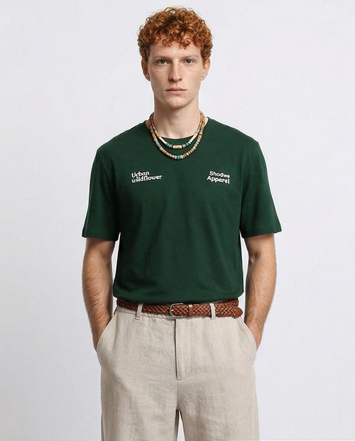 Man wearing a green t-shirt with text, standing against a plain background