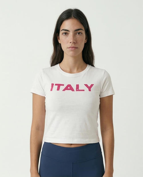 Woman wearing a white t-shirt with 'ITALY' in pink on a plain background