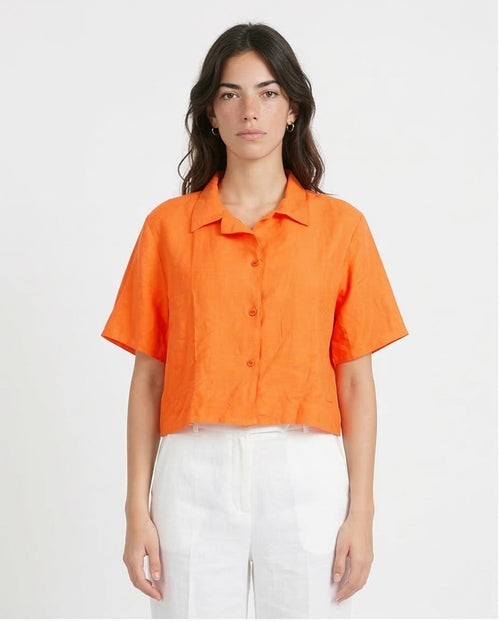Woman wearing an orange shirt and white pants on a plain background