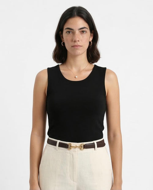 Woman wearing a black sleeveless top and white pants on a plain background