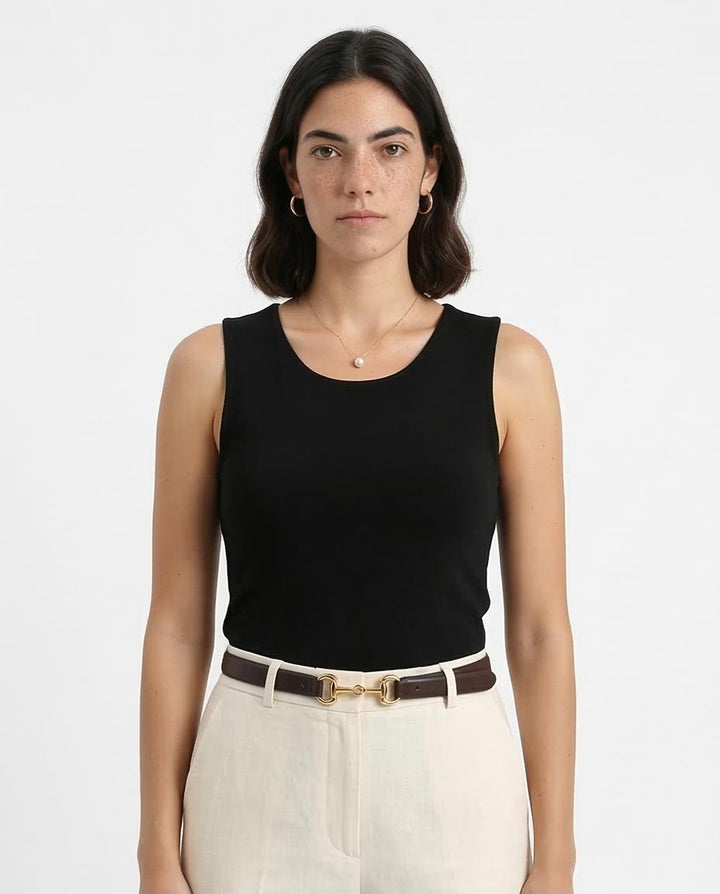Woman wearing a black sleeveless top and white pants on a plain background