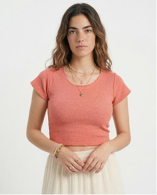 Woman wearing a coral crop top and beige skirt on a white background