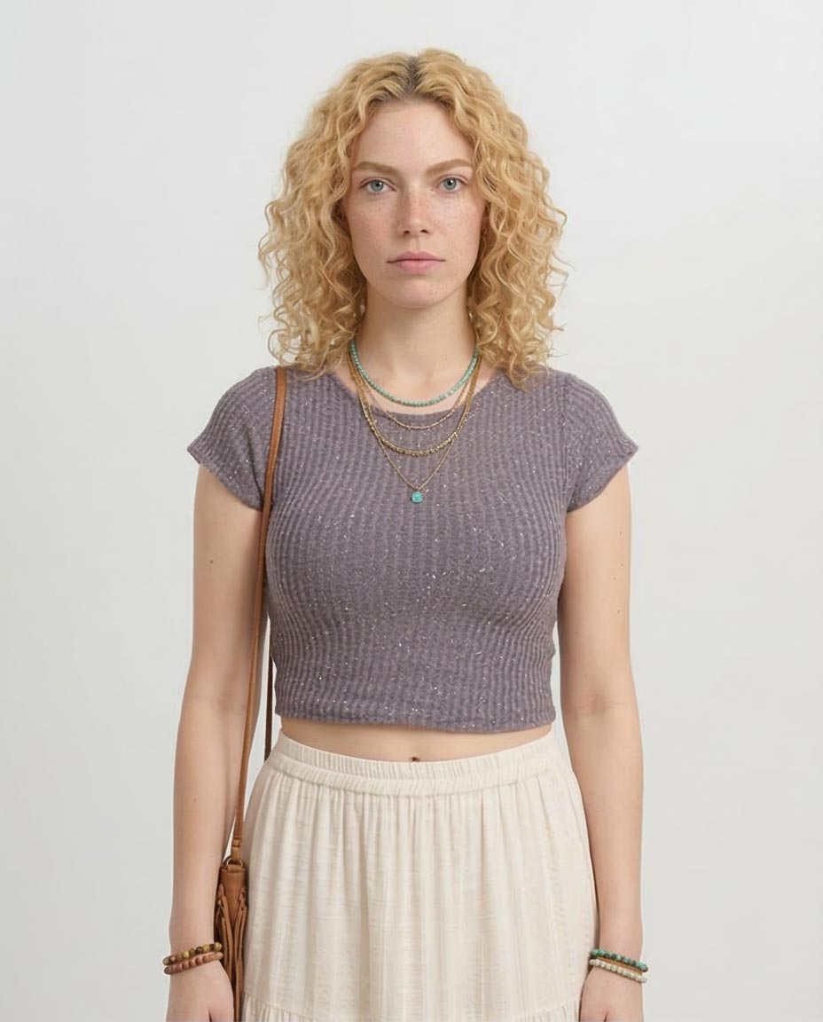 Woman wearing a purple knitted top and beige skirt against a plain background
