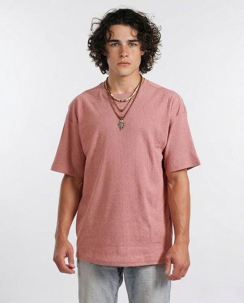 Man wearing a pink textured t-shirt and multiple necklaces on a white background