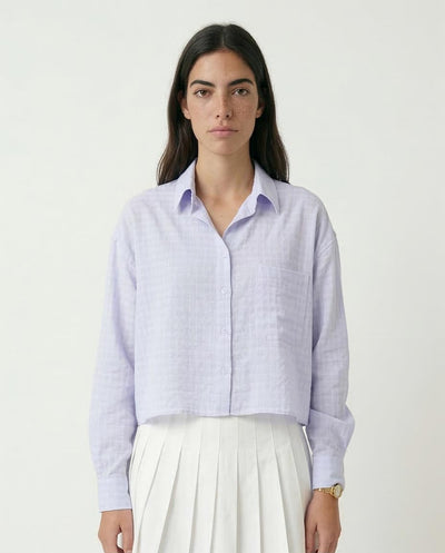 Woman wearing a light purple checkered shirt and white pants on a plain background