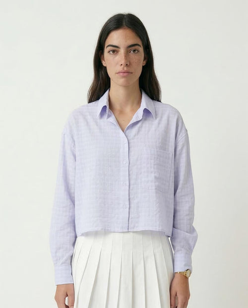 Woman wearing a light purple checkered shirt and white pants on a plain background