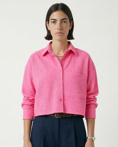 Woman wearing a pink textured shirt with navy pants on a white background
